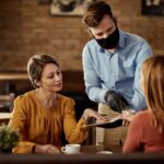 waiter wearing protective face mask while recommending something from the menu to his customers 1024x683 1