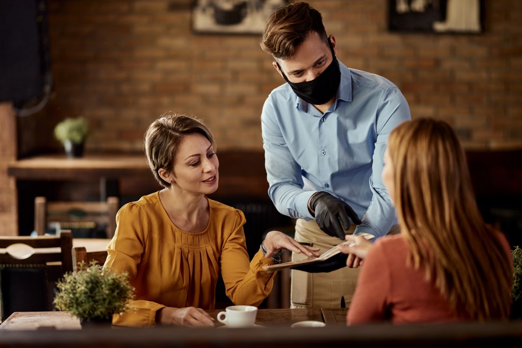 waiter wearing protective face mask while recommending something from the menu to his customers 1024x683 1
